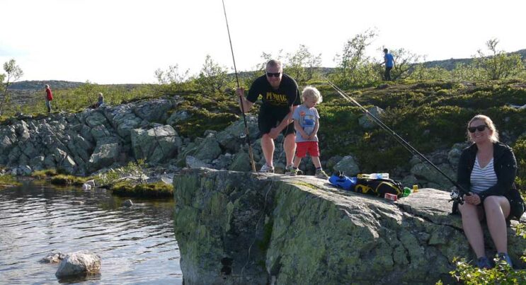 Familj som fiskar från klippor i en fjälltjärn.