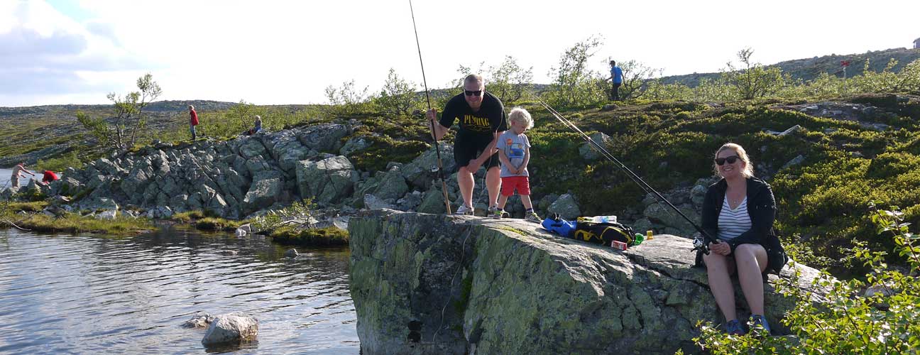 Familj som fiskar från klippor i en fjälltjärn.