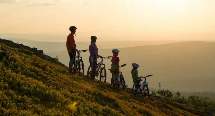 Familj med cyklar som tittar på solnedgången från fjället.