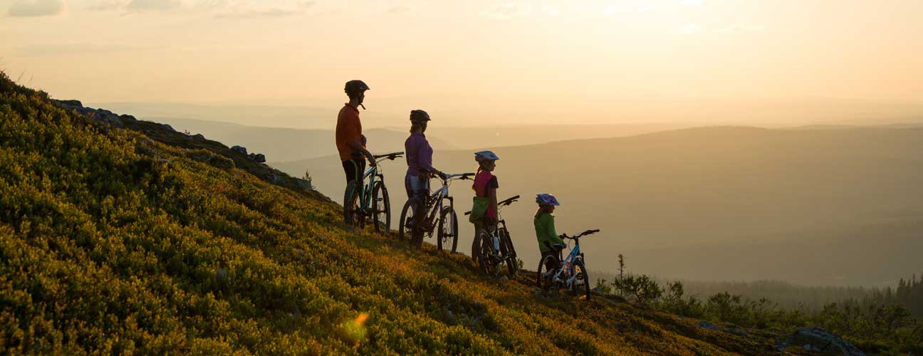 Familj med cyklar som tittar på solnedgången från fjället.