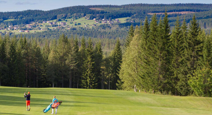 Golfbana i Vemdalen, Klövsjö by i bakgrunden och par med golfbags i förgrunden