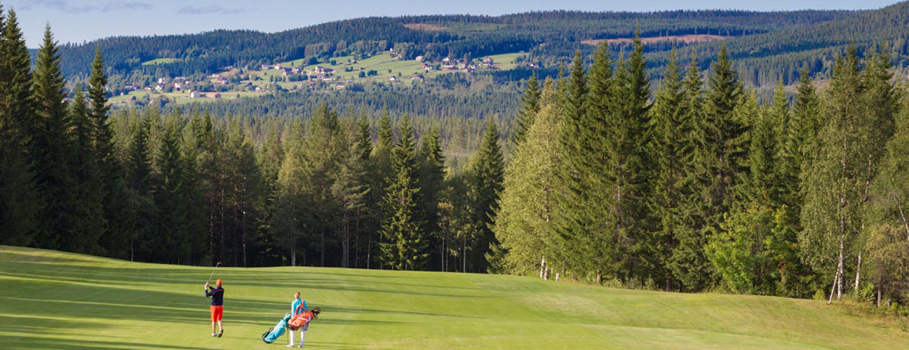 Golfbana i Vemdalen, Klövsjö by i bakgrunden och par med golfbags i förgrunden