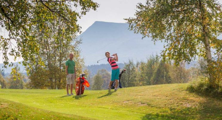 Två golfspelare med fjäll i bakgrunden.