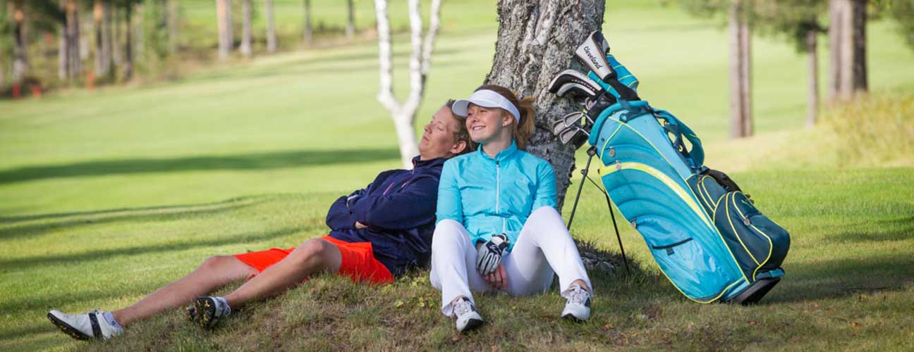 Par som sitter och vilar och lutar sig mot ett träd under en golfrunda.