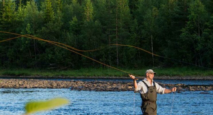 Man som flugfiskar efter harr i ett strömmande vattendrag.