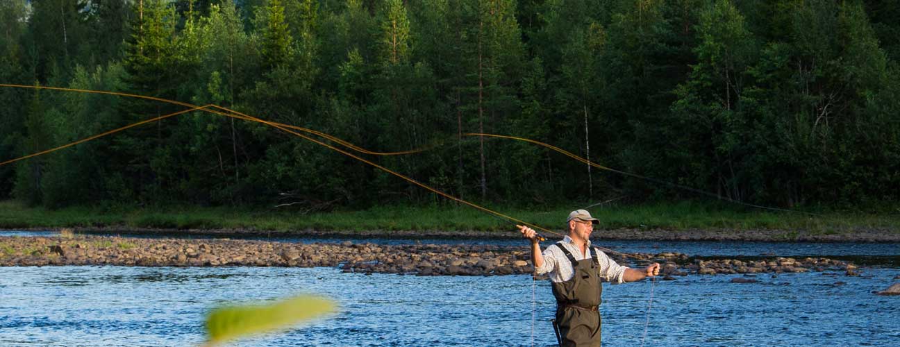 Man som flugfiskar efter harr i ett strömmande vattendrag.