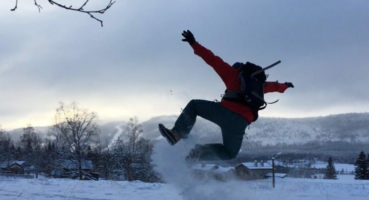 Man som hoppar i snön och gör ett hoppsasteg så att snön yr