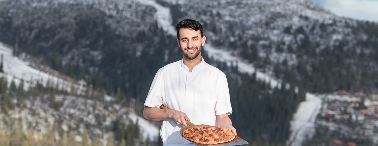 Pizzabagare framför snötäckta fjäll med pizza i Vemdalen