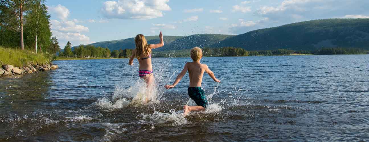 Barn som springer ut i sjön för ett dopp.