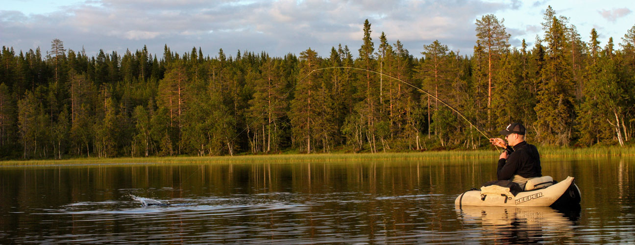 En fiskare i en liten båt i vacker skogstjärn.