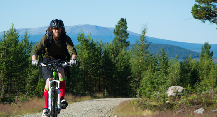 Cyklist på grusväg med fjällen i bakgrunden under sommartid