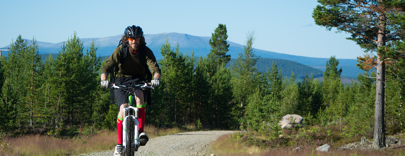 Cyklist på grusväg med fjällen i bakgrunden under sommartid