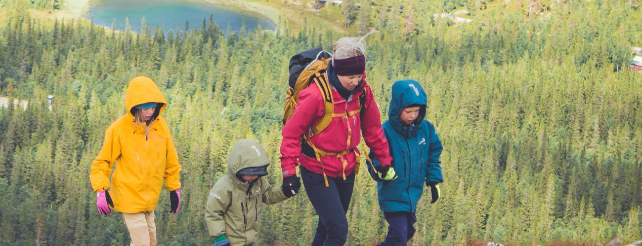 Kvinna tillsammans med tre barn bestiger Sonfjället i Härjedalen, högt uppe på berget med skog i bakgrunden.