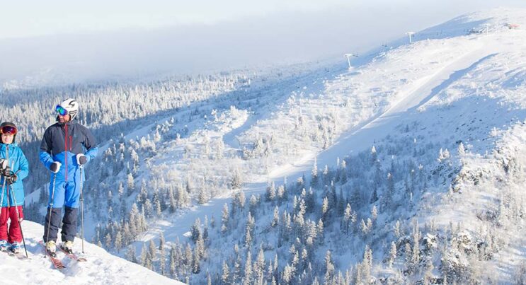 Familj på toppen av skidbacken hovdetoppen iklädda skidkläder med pjäxor, stavar och skidor.