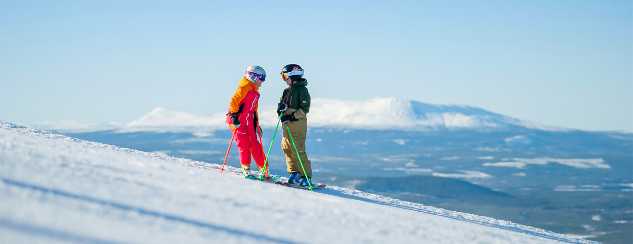 Barn som står i skidbacke fullt utrustade. Sonfjället i bakgrunden