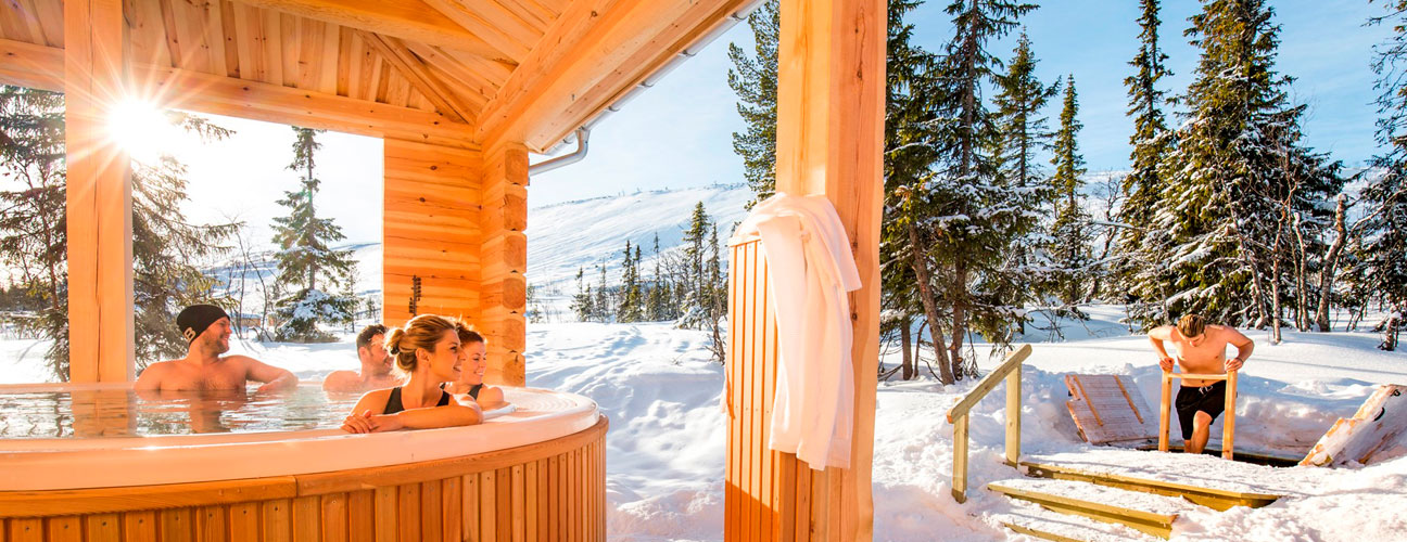 Fjällvistet Storhogna högfjällshotell och spa. sällskap badar i bubbelpool en solig vinterdag, skidbackar i bakgrunden.